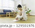 リビングのフローリングに座って靴下を足先を触る若い女性 129501976