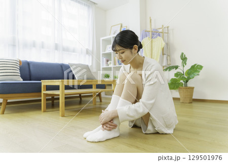 リビングのフローリングに座って靴下を足先を触る若い女性 129501976