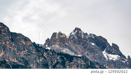 A detailed view of the Dolomite peaks shrouded in a soft white cloud. The rugged, jagged edges of the mountains contrast with the delicate mist, creating a dramatic natural scene 129502022