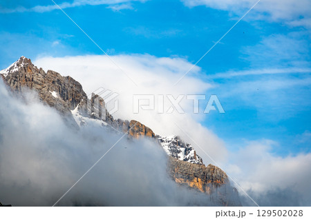 A detailed view of the Dolomite peaks shrouded in a soft white cloud. The rugged, jagged edges of the mountains contrast with the delicate mist, creating a dramatic natural scene A detailed view of the Dolomite peaks shrouded in a soft white cloud. The rugged, jagged edges of the mountains contrast with the delicate mist, creating a dramatic natural scene 129502028