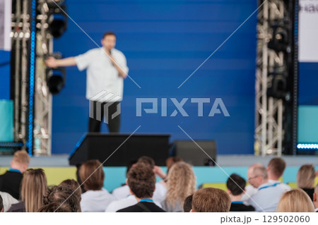 Speaker presenting to audience at professional event with blue stage backdrop Speaker presenting to audience at professional event with blue stage backdrop 129502060