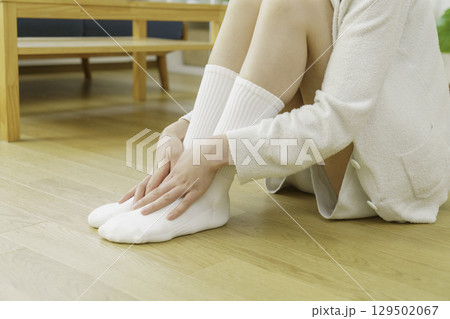 リビングのフローリングに座って足元を温める若い女性の足元のアップ 129502067