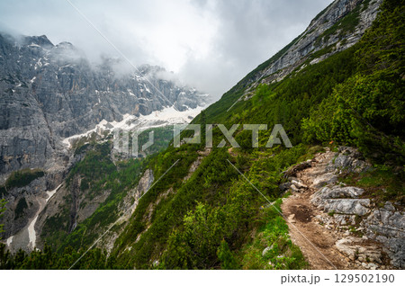 Mountain trail in the Dolomites (Dolomiti, Dolomiten), Italy, leading to Lago Sorapis. The path winds along rocky slopes with stunning views of valleys, forests, and peaks 129502190