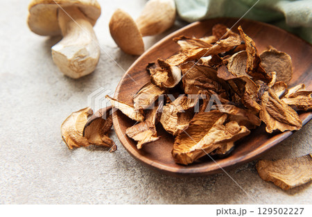 Dried porcini mushrooms resting in wooden bowl on gray textured background Dried porcini mushrooms resting in wooden bowl on gray textured background 129502227