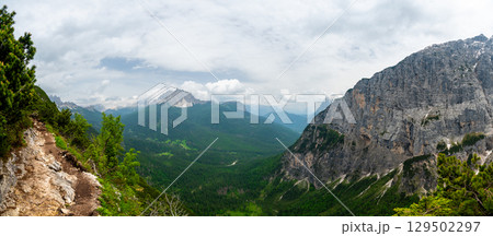 Breathtaking view of forests, mountains, and valleys in the Italian Dolomites (Dolomiti, Dolomiten). Captured from a scenic trail along a rocky ledge. Stunning alpine nature 129502297