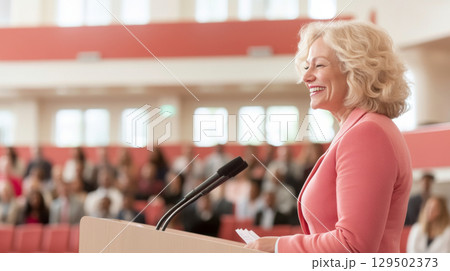 Mature woman speaking at public event with audience in background 129502373