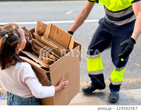 Caucasian child and municipal worker collaborating in cardboard recycling effort 129502567