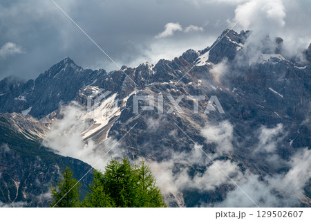 Mountain peaks around Cinque Torri in the Dolomites (Dolomiti, Dolomiten), Italy. Majestic summits partially covered in mist and clouds, with lush forests in the valleys below Mountain peaks around Cinque Torri in the Dolomites (Dolomiti, Dolomiten), Italy. Majestic summits partially covered in mist and clouds, with lush forests in the valleys below 129502607
