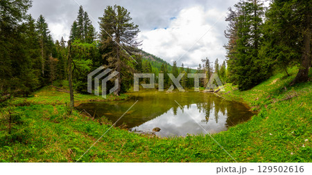 Lago Bain de Dones in the Dolomites (Dolomiti, Dolomiten), Italy. A serene alpine lake surrounded by lush forests and towering mountain peaks, reflecting the stunning natural landscape Lago Bain de Dones in the Dolomites (Dolomiti, Dolomiten), Italy. A serene alpine lake surrounded by lush forests and towering mountain peaks, reflecting the stunning natural landscape 129502616