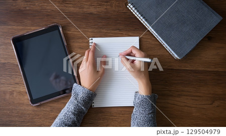overhead of hands writing notes with tablet open nearby, 129504979
