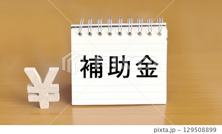 リングノートに補助金の文字と円マーク_茶色背景 129508899
