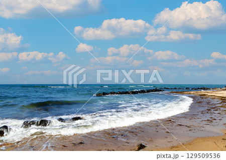 Waves on the shore of the Blue Sea and a sandy beach with blue clouds on a sunny summer day. 129509536