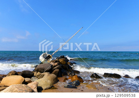 Wide sandy shore under blue sky, wrecked yacht beyond waves. 129509538