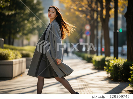 都会の黄葉並木道を颯爽と歩くグレーのコートを着たロングヘアの女性（秋コーデ） 129509743