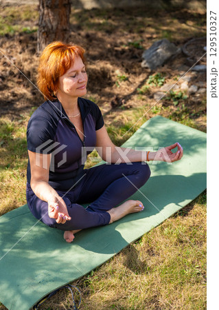 Woman meditating outdoors in a peaceful park setting during her morning routine. Mindfulness, mental balance, and emotional self-care. 129510327
