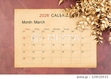 March 2026 calendar page with golden color leaves on red wooden background. 129510515