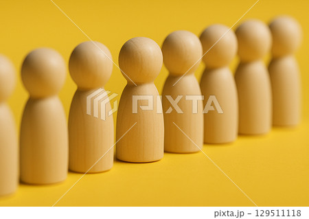 A red figurine in front of a uniform group of natural figurines symbolizing command, authority, or representation 129511118