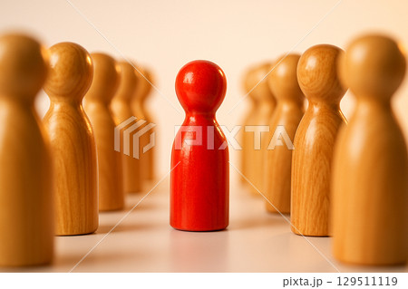 A red figurine separated from a group of natural figurines symbolizing exclusion, isolation, or detachment 129511119