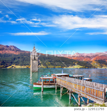 Astonishing autumn lake landscape with a ship near the pier and  submerged bell tower in lake Resia or Reschensee. 129511793
