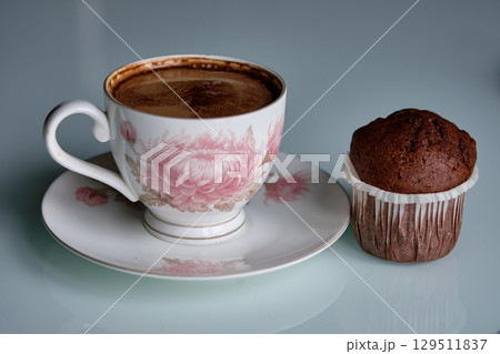 Coffee and chocolate muffin on a white table with floral patterns in a cozy setting for a delightful afternoon treat 129511837