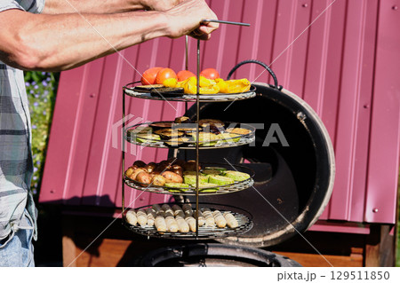 Grilling fresh vegetables and fruits on a multi-tiered grill in a backyard on a sunny day Grilling fresh vegetables and fruits on a multi-tiered grill in a backyard on a sunny day 129511850