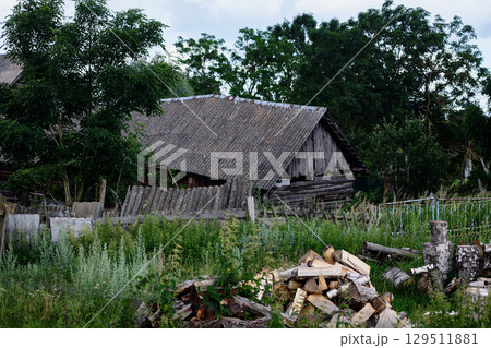 Old wooden house surrounded by overgrown grass and stacked firewood in a rural setting Old wooden house surrounded by overgrown grass and stacked firewood in a rural setting 129511881