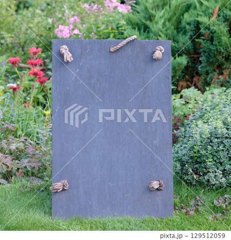 Garden display board made of slate in an outdoor setting surrounded by colorful flowers and greenery. Copy space. Garden display board made of slate in an outdoor setting surrounded by colorful flowers and greenery. Copy space. 129512059