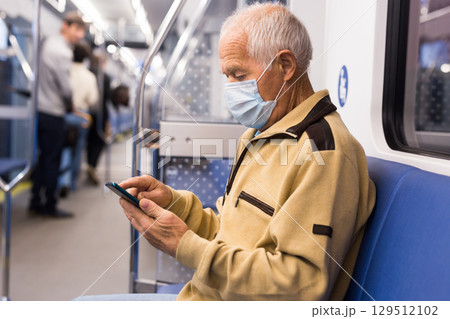 Elderly man in mask in subway car with smartphone Elderly man in mask in subway car with smartphone 129512102