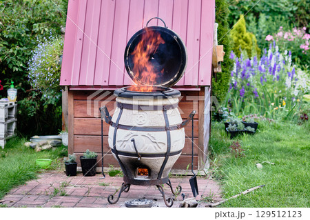 Fire erupting from a traditional outdoor clay stove in a vibrant garden on a sunny day Fire erupting from a traditional outdoor clay stove in a vibrant garden on a sunny day 129512123