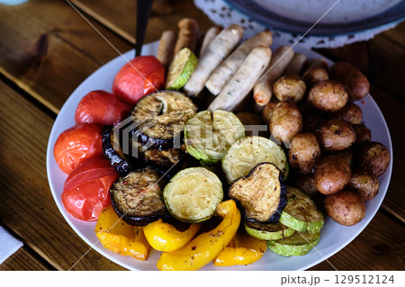 Colorful platter of grilled vegetables and sausages served at a rustic outdoor setting during a summer gathering Colorful platter of grilled vegetables and sausages served at a rustic outdoor setting during a summer gathering 129512124