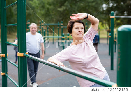 elderly woman doing exercises on a horizontal bar at an outdoor sports ground elderly woman doing exercises on a horizontal bar at an outdoor sports ground 129512126