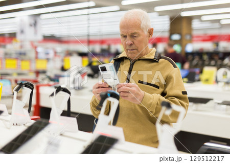 elderly man examines tablet computer in showroom of electronics store elderly man examines tablet computer in showroom of electronics store 129512217