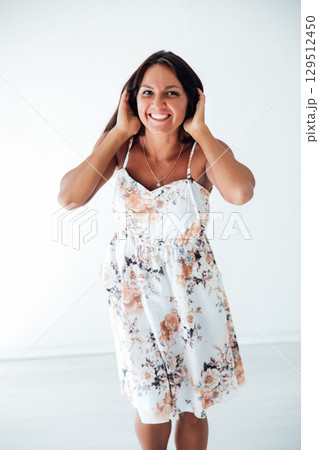 Tanned brunette woman in white summer dress holding her hair with her hands and smiling 129512450
