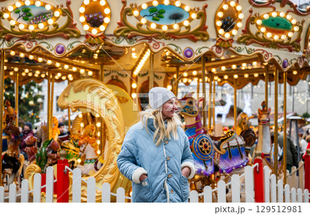 Smiling woman in blue coat standing in front of carousel at Christmas market in Tallinn Smiling woman in blue coat standing in front of carousel at Christmas market in Tallinn 129512981