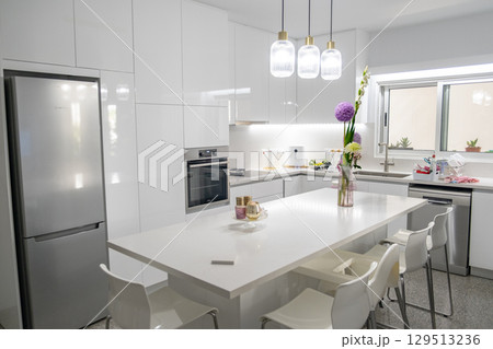Sleek White Kitchen with Island, Pendant Lights, and Floral Decor Sleek White Kitchen with Island, Pendant Lights, and Floral Decor 129513236