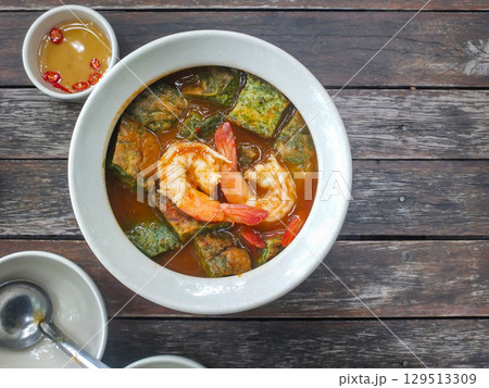 Thai food: Cha-om egg curry with shrimp in a white bowl on a wooden table. 129513309