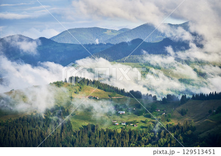 Picturesque scene of mountain valley blanketed in mist, with patches of green pastures and scattered houses. Clouds drift gently over forested hills, creating serene and tranquil atmosphere. Picturesque scene of mountain valley blanketed in mist, with patches of green pastures and scattered houses. Clouds drift gently over forested hills, creating serene and tranquil atmosphere. 129513451