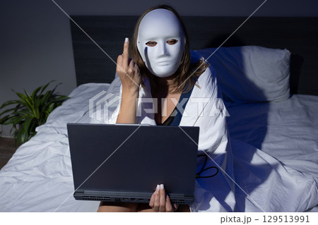 Digital Privacy Risks Illustrated by Masked Figure in Bed With Laptop at Night 129513991