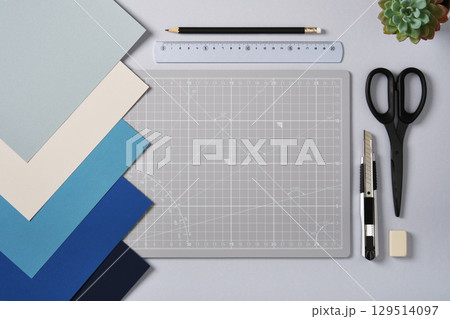 Craft tools, blue-tinted colored paper, and a cutting mat on the table. A creative workspace with space for your text. 129514097
