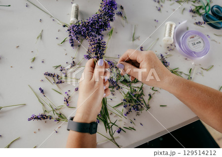 First-person view: florist carefully arranging bouquet of fresh lavender on white table, using ribbon, and wire, creating fragrant and beautiful arrangement. Skilled florist arranging lavender bouquet First-person view: florist carefully arranging bouquet of fresh lavender on white table, using ribbon, and wire, creating fragrant and beautiful arrangement. Skilled florist arranging lavender bouquet 129514212