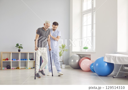 Portrait of young nurse helping a senior patient to walk with his crutches in rehabilitation clinic Portrait of young nurse helping a senior patient to walk with his crutches in rehabilitation clinic 129514310