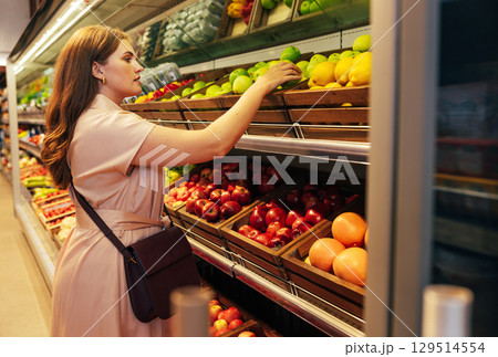 Young woman customer takes out a green apple from the shelf in the grocery store 129514554