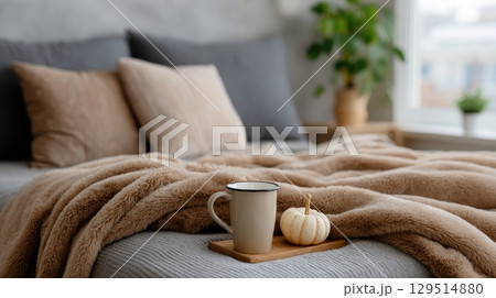 A warm bedroom features soft pillows and a cozy blanket, complemented by a mug of hot cocoa, perfect for autumn relaxation 129514880