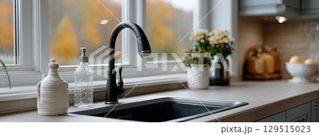 A minimalist kitchen showcases a sleek black faucet and white countertop, with autumn colors visible through the window 129515023