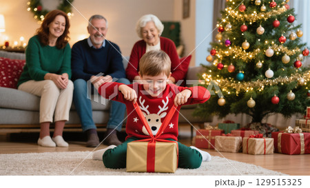 Christmas morning with a smiling boy opening a gift while family watches near a decorated festive tree 129515325