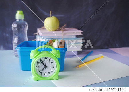 Back to school concept, school food. Lunch box with healthy sandwich, alarm clock, stack of books, apple and bottle of water on chalkboard background. 129515544