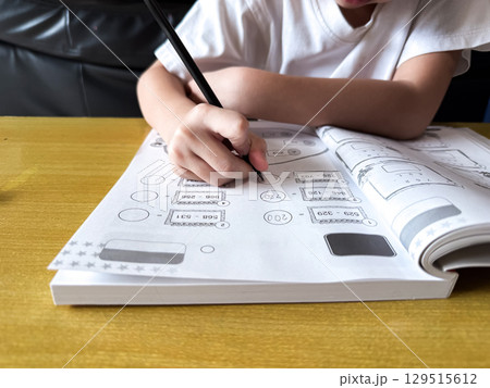 A young student sits at a wooden desk working on basic math exercises, steadily developing essential problem solving skills. A young student sits at a wooden desk working on basic math exercises, steadily developing essential problem solving skills. 129515612