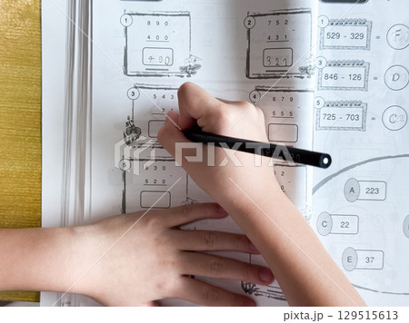A young student sits at a wooden desk working on basic math exercises, steadily developing essential problem solving skills. A young student sits at a wooden desk working on basic math exercises, steadily developing essential problem solving skills. 129515613