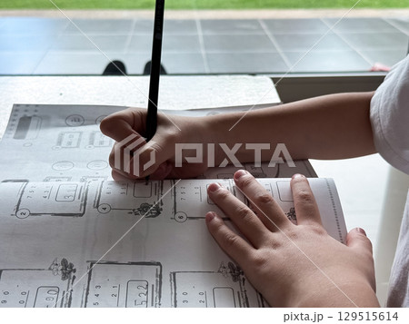 A young student sits at a wooden desk working on basic math exercises, steadily developing essential problem solving skills. A young student sits at a wooden desk working on basic math exercises, steadily developing essential problem solving skills. 129515614