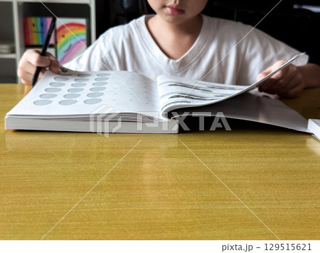 A young student sits at a wooden desk working on basic math exercises, steadily developing essential problem solving skills. A young student sits at a wooden desk working on basic math exercises, steadily developing essential problem solving skills. 129515621